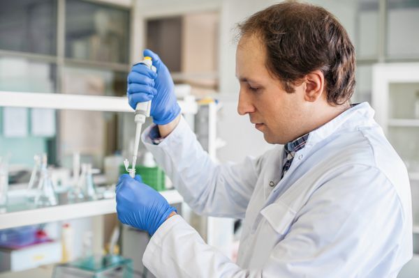 دانشمند مرد در آزمایشگاه پزشکی لوله های آزمایشگاهی را با پیپت پر می کند نزدیک