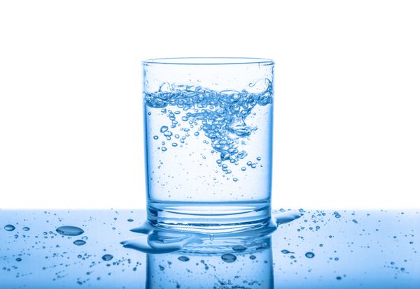 آب در شیشه شفاف با قطره و حباب جدا شده بر روی زمینه سفید پس زمینه آبی نزدیک است