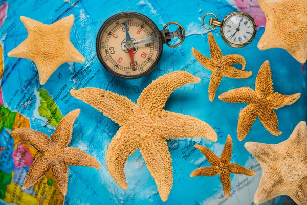 اقلام سفر یک قطب نما یک ساعت جیبی با یک زنجیر در پس زمینه یک ستاره و ستاره دریایی