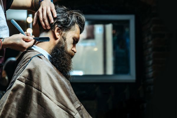 مرد ریش دار با ریش بلند وحشیانه هپسای کاکائو با سبیل گرفتن موهای شیک مو با تیغ مخصوص توسط سلمانی یا آرایشگر در آرایشگاه