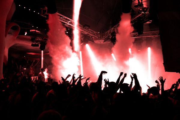 افراد حزب DJ DJ از صدای موسیقی با نور رنگی با ماشین دود و چراغ نشان می دهند دست ها را در زمین بگذار مخاطبان در کنسرت در باشگاه شب پس زمینه تاریک