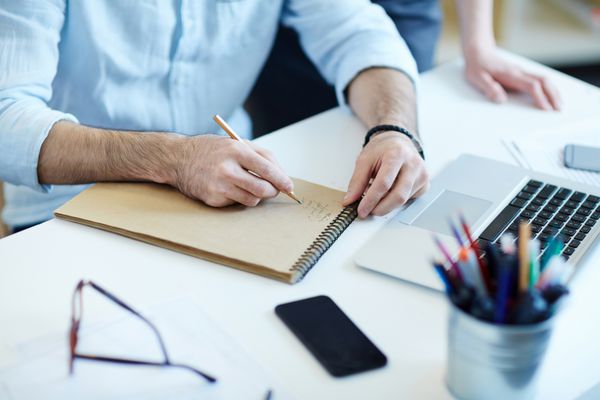 شات نزدیک از دست مردان نوشتن در دفتر یادداشت در حالی که کار در میز در دفتر