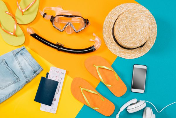 دید کلی از لباس فلیپ فلاپ بلیط هدفون گوشی هوشمند و تجهیزات snorkeling در پس زمینه رنگی آماده برای تعطیلات تابستانی