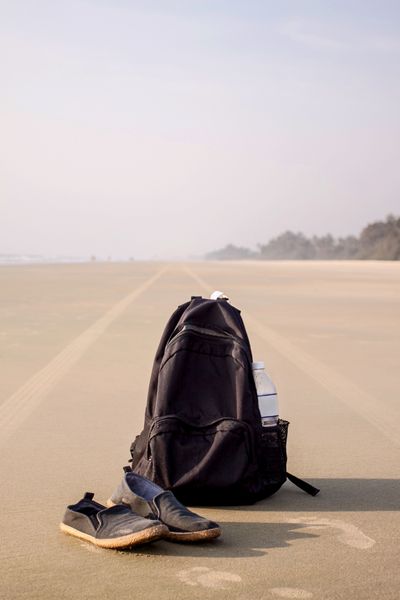 کوله پشتی سیاه و جفت کفش در ساحل ماسه