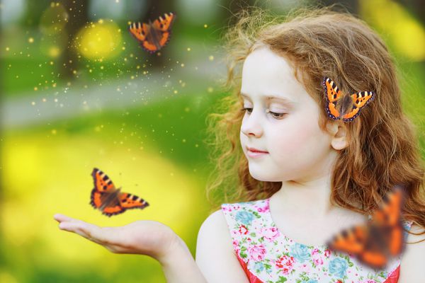 دختر فرفری زیبا با یک پروانه بر روی موهایش مفهوم مبارک کودکی