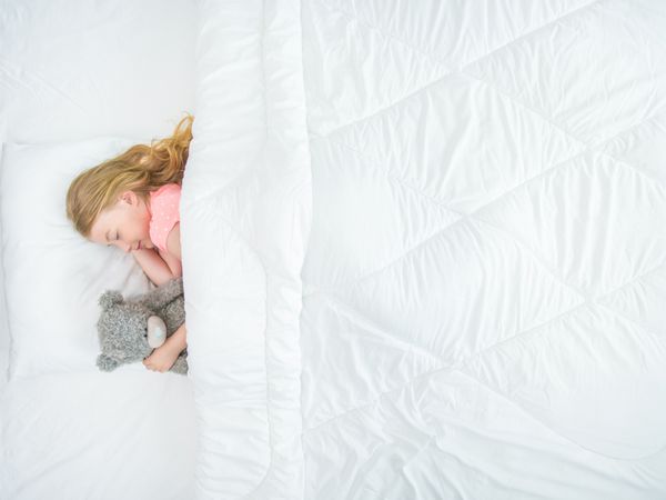 دختر کوچک با یک اسباب بازی نرم در رختخواب خوابید مشاهده از بالا
