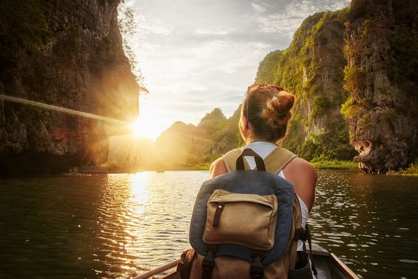 زن مبارک با کوله پشتی مسافرت با قایق با بهره گیری از غروب خورشید در میان کوه های کاروست در شمال ویتنام سفر و شیوه زندگی فعال مفهوم تعطیلات تابستانی