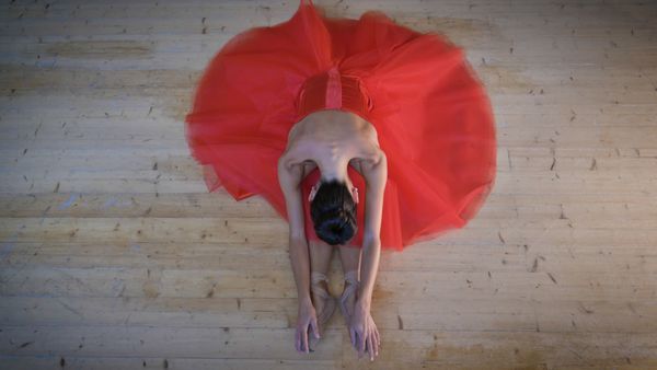 پرتره ballerina نور زیبا در یک لباس قرمز سرسبز نشسته در یک طبقه چوبی انعطاف پذیر نمایش بالا مفهوم باله زنان رژیم غذایی نازک شکل زیبا سبک زندگی سالم انعطاف پذیری