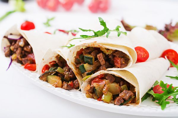 Burritos با گوشت گاو و سبزیجات در یک پس زمینه نور پیچیده می شود