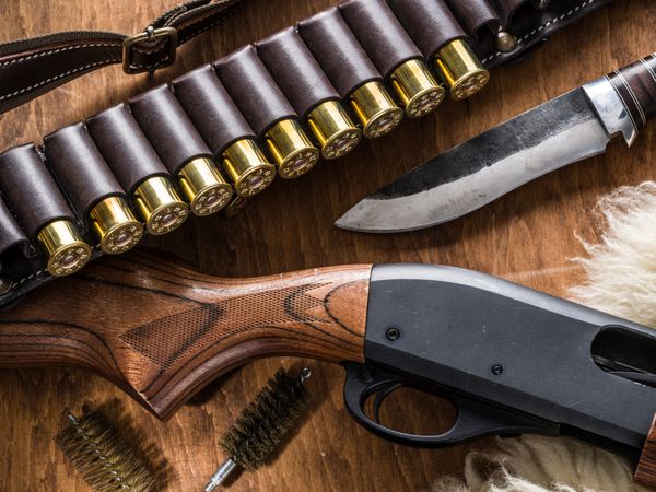 تجهیزات شکار تفنگ ساچمهای پمپ کارتریج شکار 12 میلیمتری و چاقو شکار بر روی میز چوبی
