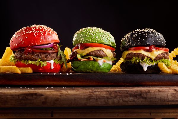 سه همبرگرهای نان رنگارنگ رنگی در قرمز سبز و سیاه ارائه گزینه های مختلف برای پر کردن مشاهده از طرف در هیئت مدیره چوبی