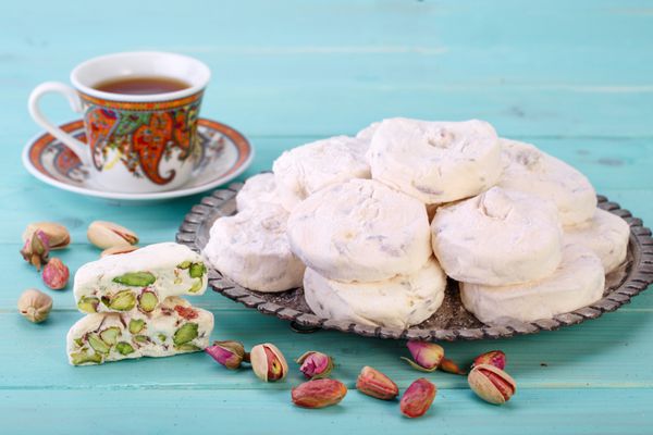 شکلات های شیرین نرگس سفید سفال ایرانی و ایرانی با آجیل پسته از شهر اصفهان و یک فنجان چای در پس زمینه چوب فیروزه ای آبی