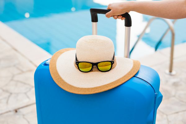 مفهوم سفر تعطیلات و تعطیلات چمدان آبی کلاه و عینک آفتابی در نزدیکی استخر