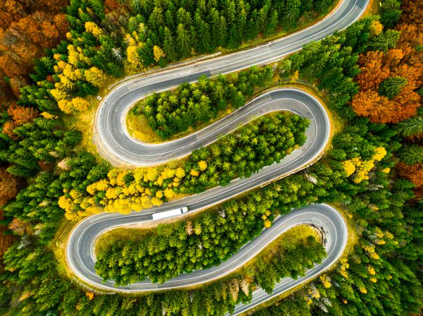 دید هوایی از کامیون راه خود را بر روی یک جاده انحنا از طریق جنگل های رنگارنگ پاییز