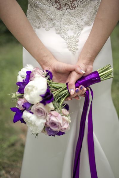 دست های خود را پشت سر گذاشته دسته کوچک عروسی کمی از گل های رز را با نوارهای بنفش نگه داشته اند