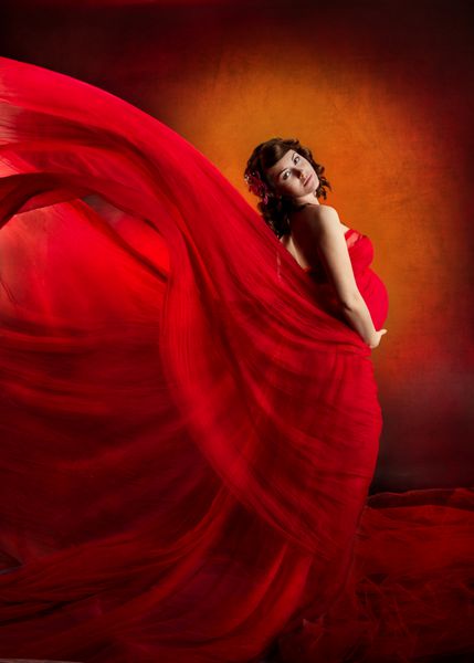 زن باردار در لباس قرمز وحشت زده با پرواز در جریان باد