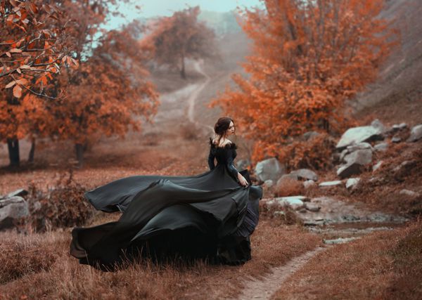 دختر خیره کننده باور نکردنی در یک لباس سیاه پس زمینه پاییز فوق العاده است عکاسی هنری