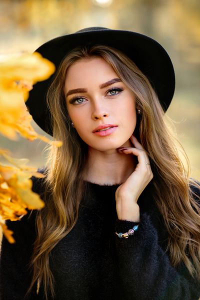 یک عکس زیبا از یک دختر زیبا در یک لباس تاریک و کلاه سیاه که در نزدیکی برگ های رنگارنگ پاییز ایستاده است را بست کار هنری زن رمانتیک مدل تندرستی ملایم به دوربین