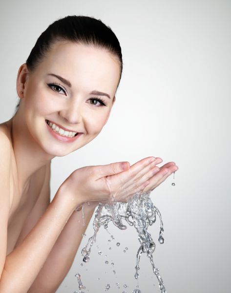 زن جوان زیبا لبخند زدن شستن صورت خود را با آب شات استودیو