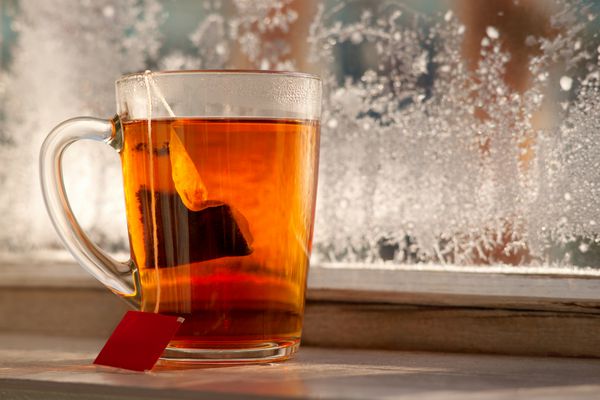 یک کیسه چای در یک لیوان یک لیوان چای بر روی پنجره بالکن در زمستان سرد در شیشه یخ زده است الگوهای چای و سرماخوردگی یک فنجان چای در زمستان در برابر پس زمینه برف
