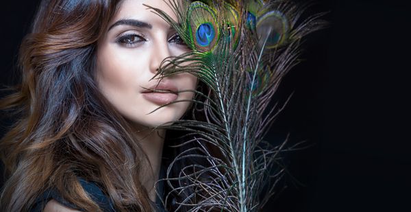 پرتره زیبا از زن جذاب با آرایش زرق و برق و پرهای طاووس