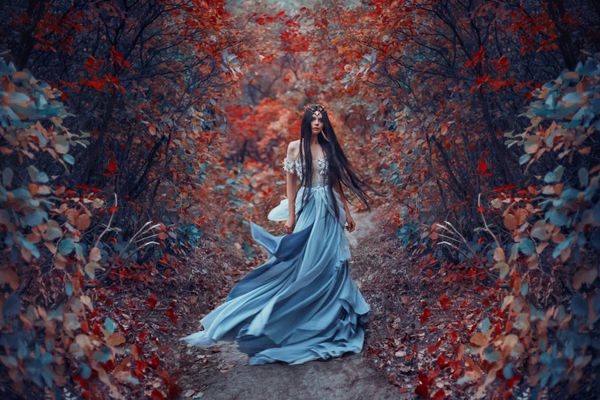 جادوگر اسرارآمیز در لباس آبی زیبا مو و لباس او در حال باد لرزیدن پس زمینه روشن پاییز جنگل آتشین با صداهای سرد عکاسی هنری