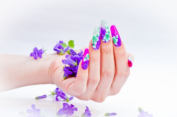 دست با ناخن های بازسازی شده و تزئین شده با گل های رنگارنگ گل های آبی و سفید بر روی زمینه سفید زیبا برای فصل بهار و تابستان