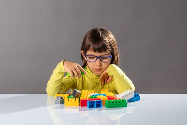 کودک با عینک های با بلوک های ساختمان یاد می گیرد فکر می کند در مورد سازماندهی اسباب بازی ها با تخیل در فضای باز