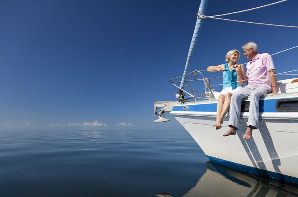 یک زن و شوهر ارشد نشسته در مقابل یک قایق بادبانی در یک دریا آبی آرام است