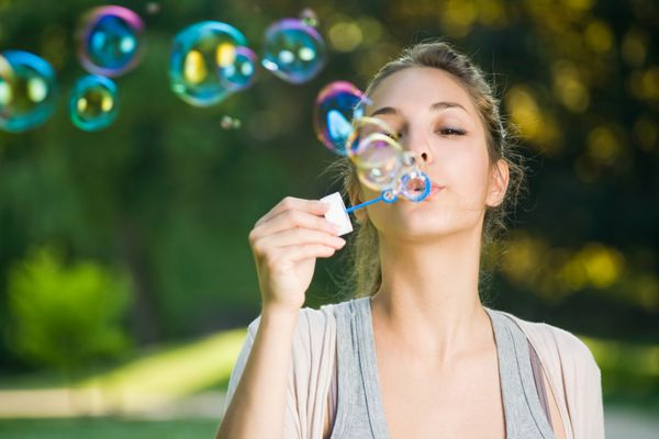 دختر جوان زیبا دمیدن حباب های صابون در خارج از منزل