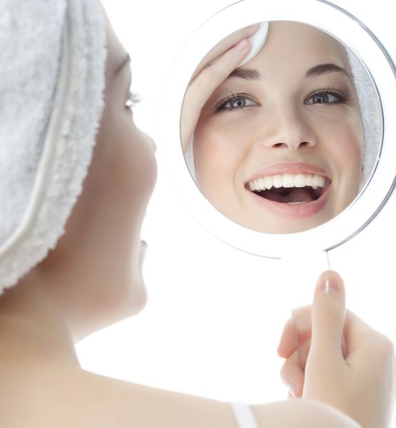 عکسی از زن زیبا لبخند زن مخفی جدا شده بر روی استودیو سفید شات تمیز کردن صورت خود را به آینه نگاه کنید