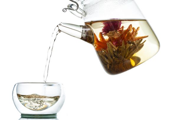ریختن چای از گلدان شیشه ای به لیوان روی زمینه سفید