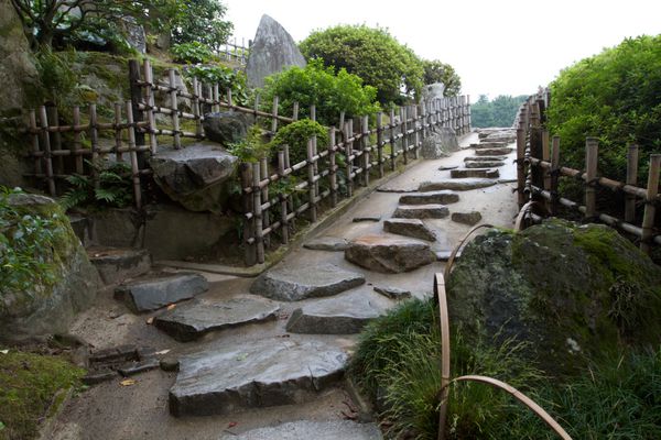 Stepping stone path bordered by bamboo fence ascends slope in Japan