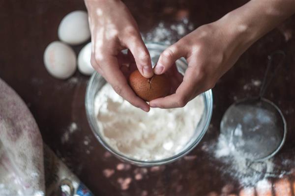 شکستن تخم مرغ روی آرد درحال پختن کیک