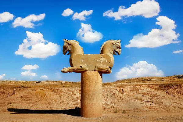 مجسمه سنگی یک گریفین در تخت جمشید در برابر یک آسمان آبی با ابرها نماد پیروزی پادشاهی باستان هخامنشی ایران پارس شیراز
