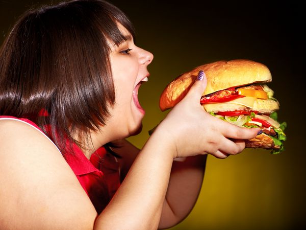 زن گرسنه با اضافه وزن که همبرگر را می خورد