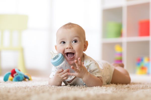 پسر بچه ناز که از بطری در حال نوشیدن است بچه خوابیدن روی فرش در مهد کودک در خانه کودک لبخند 7 ماه دارد