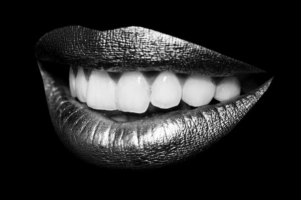 نمای نزدیک از لبهای طلایی باز و زیبا با دندانهای سفید جدا شده در پس زمینه سیاه تصویر افقی