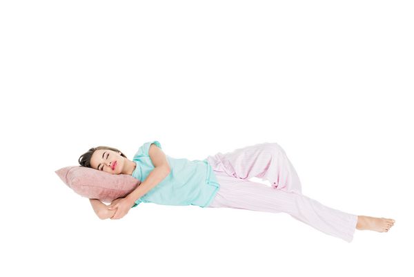 زن جوان در لباس خواب که روی بالش جدا شده روی رنگ سفید خوابیده است