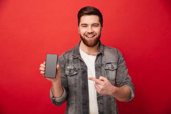 تصویر مرد جوانی که انگشت خود را روی گوشی هوشمند نشان می دهد و لبخند بر روی دوربین جدا شده بر روی زمینه قرمز