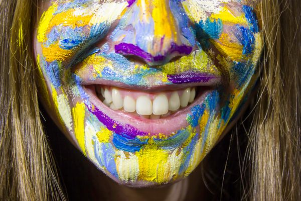 پرتره زن جوان زیبا با نقاشی رنگی روغن روی صورت لبخند نزدیک مفهوم خدمات دندانپزشکی