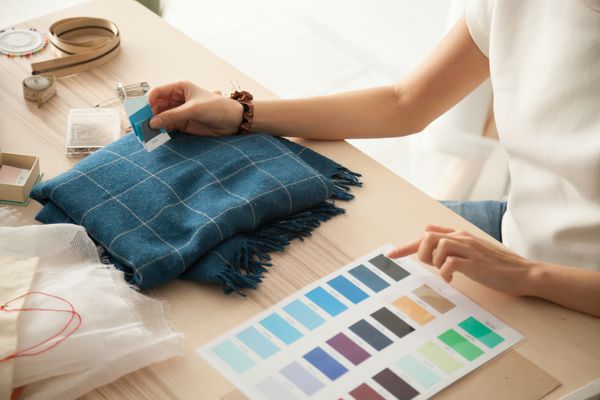 طراح مد زن که نمونه رنگی را انتخاب می کند سایه های آبی پارچه ای پارچه ای را در محل کار پیراهن خیاطی یا خیاط کار در میز کار نشان می دهد که در انتخاب پالت انتخاب انتخاب نمای نزدیک