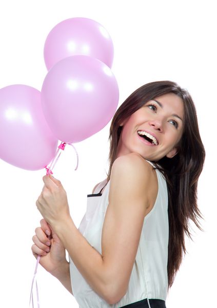 دختر جوان با بالن صورتی به عنوان هدیه ای برای جشن تولد که لبخند می زند و گوشه ای را با زمینه سفید نگاه می کند