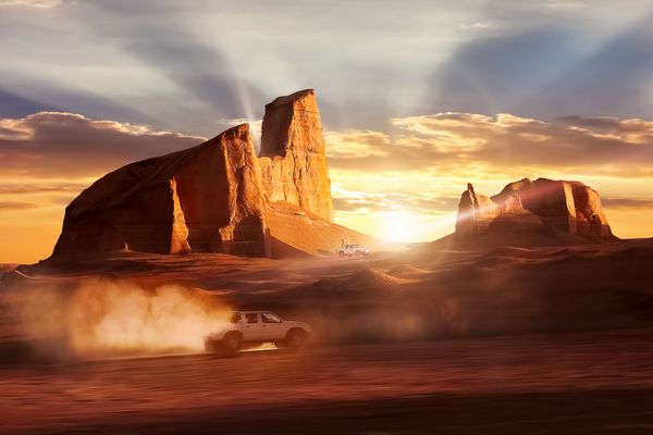 اتومبیل در حال حرکت در صحرای دشت لوت در مقابل غروب خورشید پرتوهای زیبا در زیر صخره ها ایران کرمان پارس