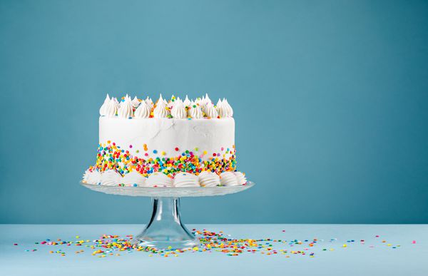 کیک تولد سفید با آبپاش های رنگارنگ بر روی یک پس زمینه آبی
