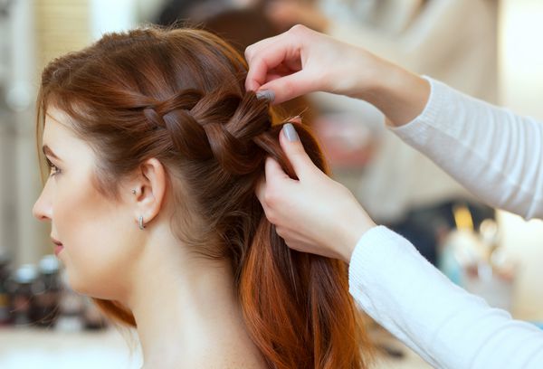 دختر زیبا و موی قرمز با موهای بلند آرایشگاه بافته می شود یک تسمه فرانسوی در یک سالن زیبایی مراقبت از مو حرفه ای و ایجاد مدل مو