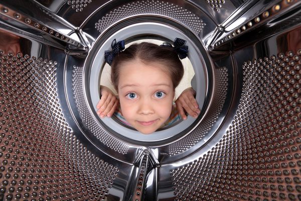یک دختر بچه کنجکاو به ماشین لباسشویی خالی طبل نگاه می کند