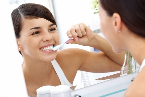 تصویری از زن زیبا که هنگام صبح دندان های خود را جلوی آینه می کند