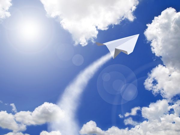 هواپیمای کاغذی که در برابر آسمان آبی پرواز می کند