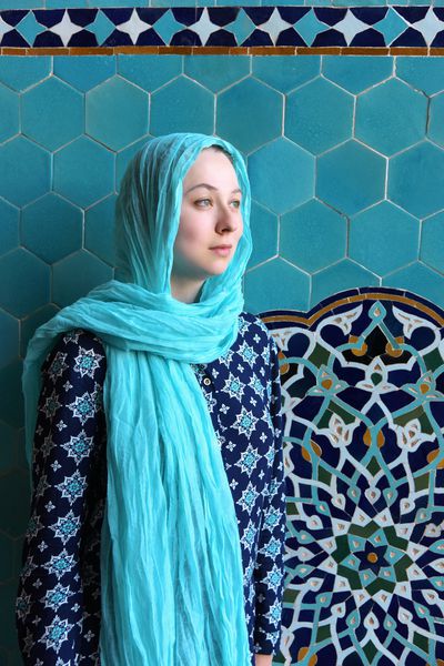 زن جوان توریستی با لباس مسلمان در کنار مسجد نما این زن با شال و لباس آبی به سبک سنتی ایرانی است یزد ایران